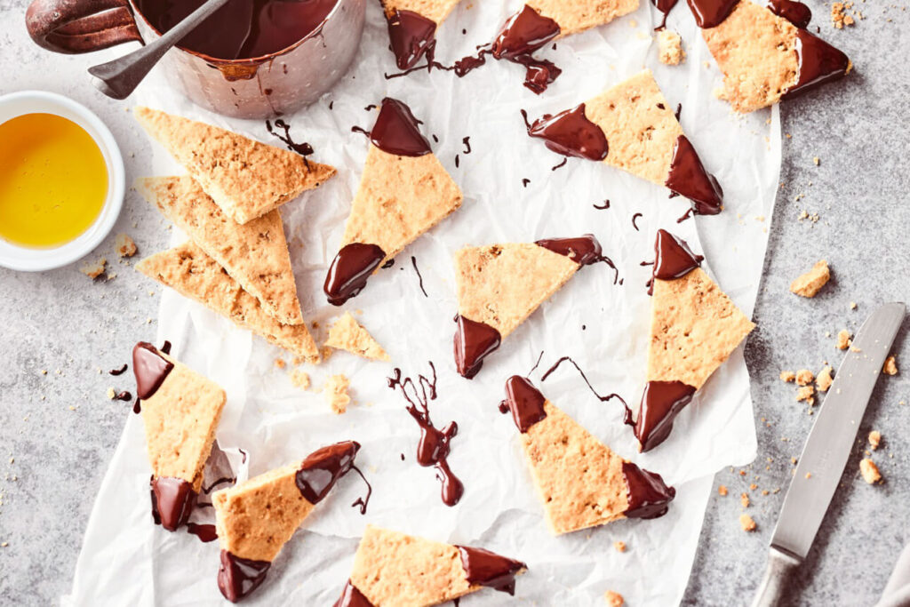 Bakpapier met knapperige honinghoekjes, een schaaltje honing en een bakje gesmolten chocolade ernaast