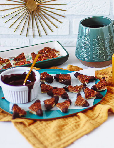 Op een bord liggen een heleboel mini notenhoekjes omhuld met chocolade en een kommetje gesmolten chocolade.