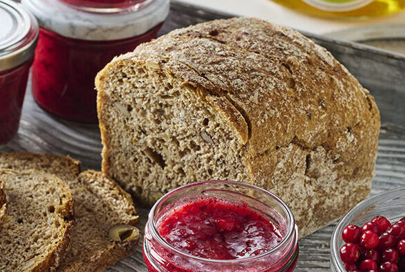 Op een dienblad ligt een sneetje brood met boter, omringd door verschillende potjes honing en cranberryjam en een schaaltje verse cranberry's.